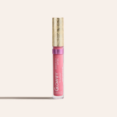 Pink sheer silk lip oil in a clear tube with a gold decorative cap standing upright