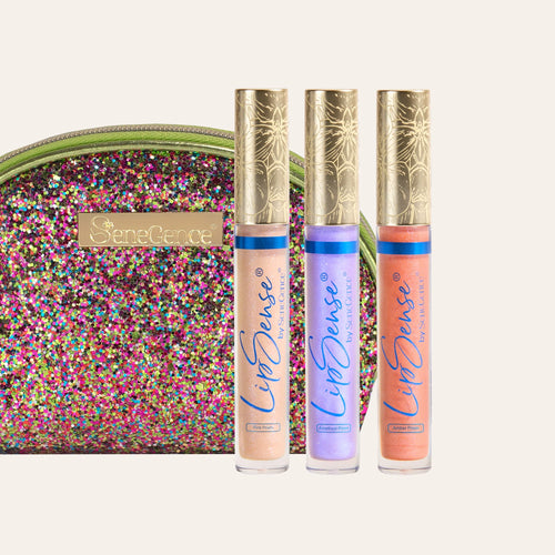 Three LipSense gloss tubes with ornate gold caps in front of a multicolored glitter clutch